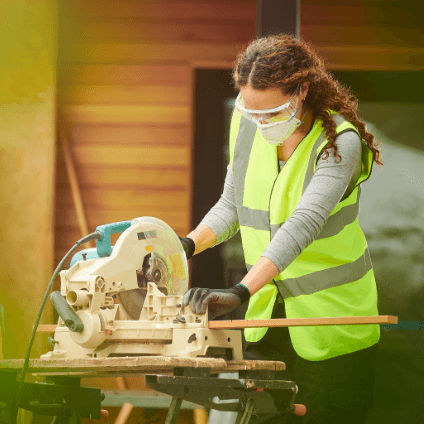 A woman wearing safety equipment and operating a miter saw
