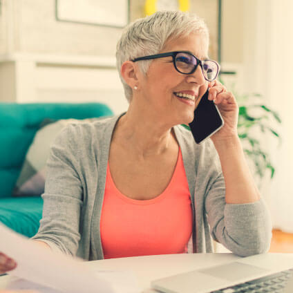 smiling woman talking on smartphone at a desk with a laptop open